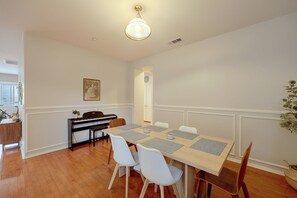 Comedor con piano, sillas blancas y una mesa con manteles individuales.