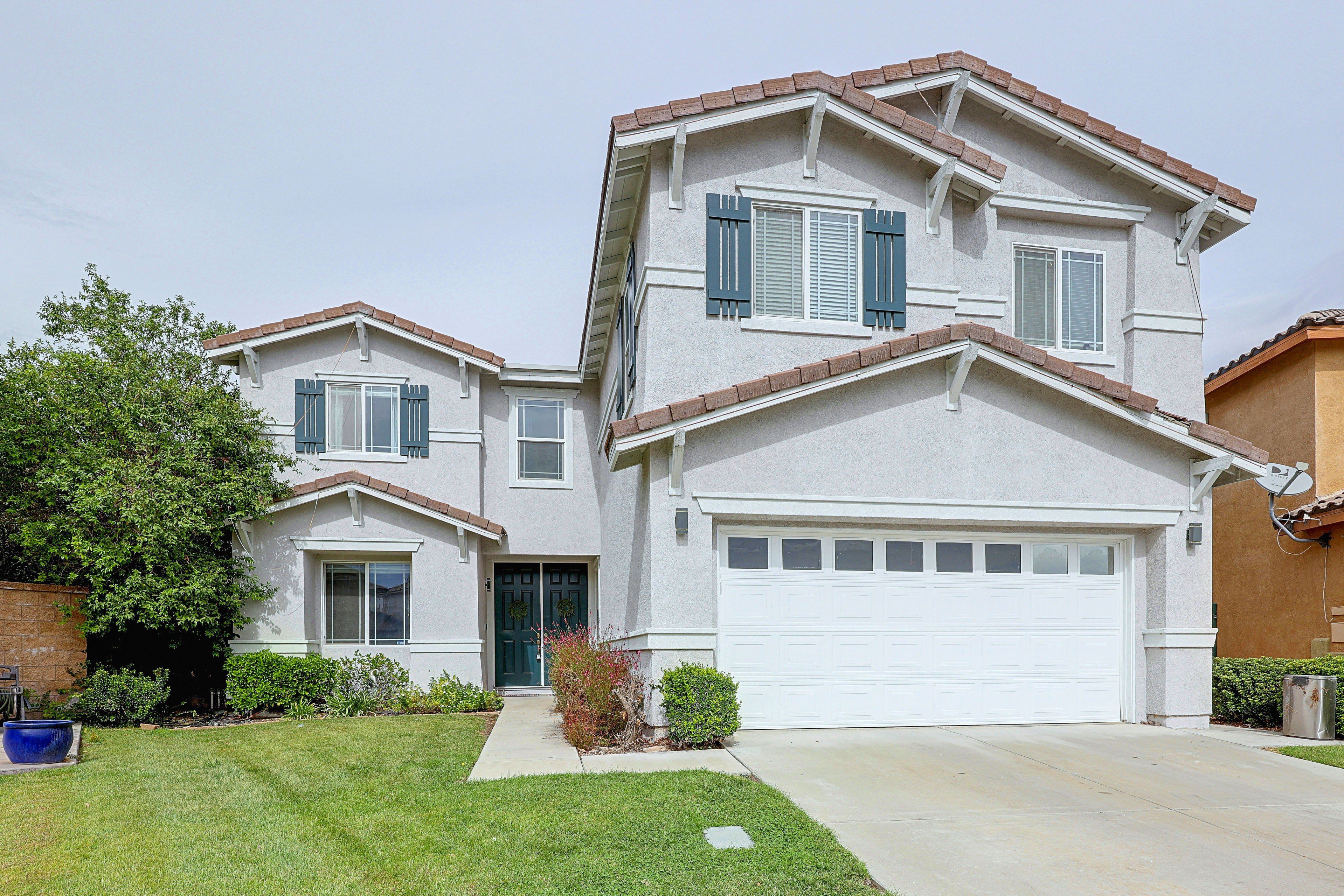 A two-story residential building with a garage, a front door, and a small front yard with a lawn and a tree.