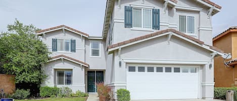 A two-story residential building with a garage, a front door, and a small front yard with a lawn and a tree.
