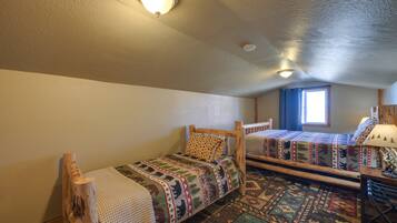 A room with two wooden beds, a window with blue curtains, and a lamp on a wooden table.