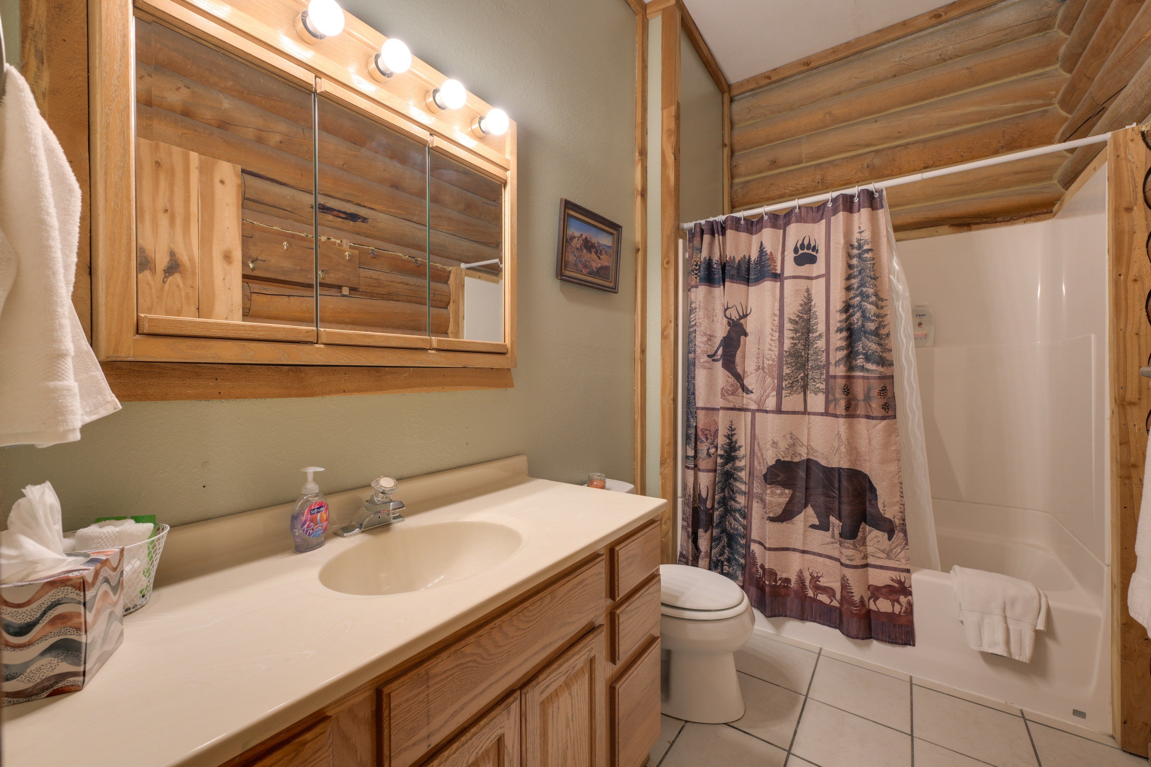 A bathroom with a wooden vanity, a mirror with lights, a sink, a toilet, and a shower curtain with animal prints.