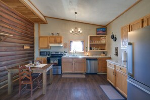 A log cabin-style kitchen with wooden cabinets, a stainless steel refrigerator, and a dining table with chairs. - Mountain Views! Peaceful Dillon Cabin w/ Yard (Dillon)