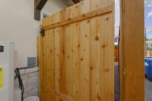 Una puerta de madera con un pestillo metálico, un cuadro eléctrico blanco y un muro de ladrillo.