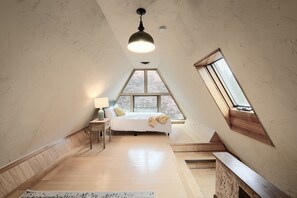 A bedroom with a sloped ceiling, a bed, a nightstand, a lamp, and a window.