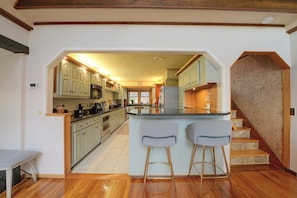 A kitchen with a central island, bar stools, and a staircase leading to another level.