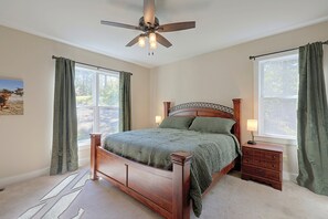 A bedroom with a wooden bed, a nightstand, a lamp, a ceiling fan, and a window with curtains.