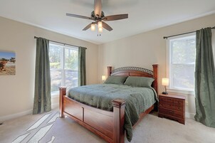 Quarto com cama de madeira, mesa de cabeceira, abajur, ventoinha no teto e janela com cortinas.