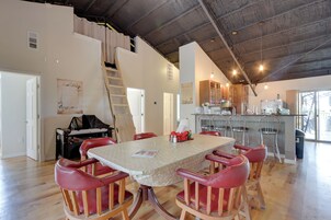Un comedor con techo de madera alto, una cocina al fondo y una escalera que lleva a un nivel superior.