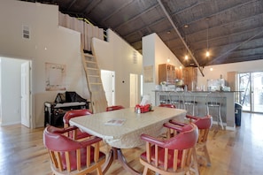 Un comedor con techo de madera alto, una cocina al fondo y una escalera que lleva a un nivel superior.