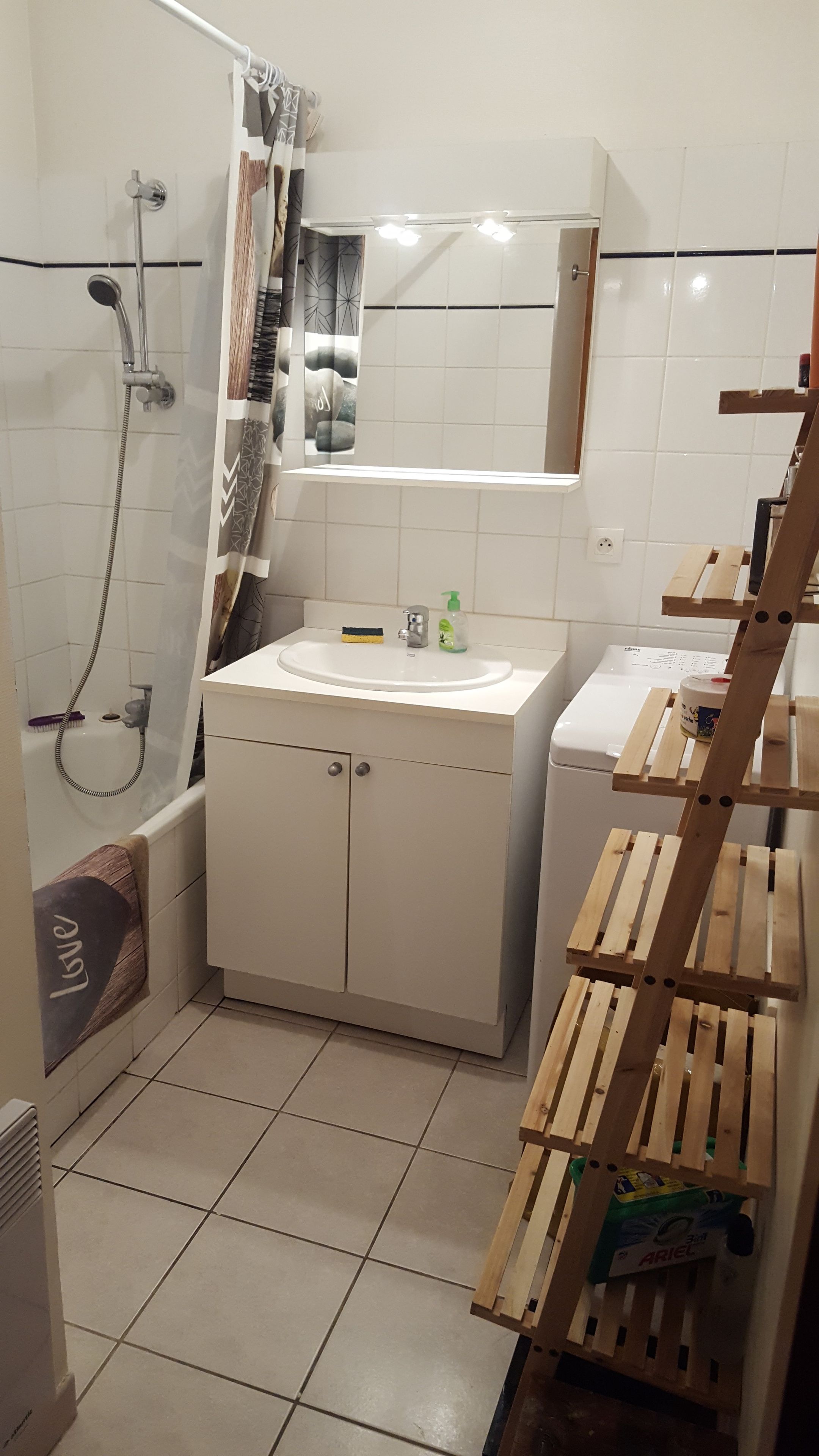 Een badkamer met een douche, wastafel, spiegel en een houten rek.