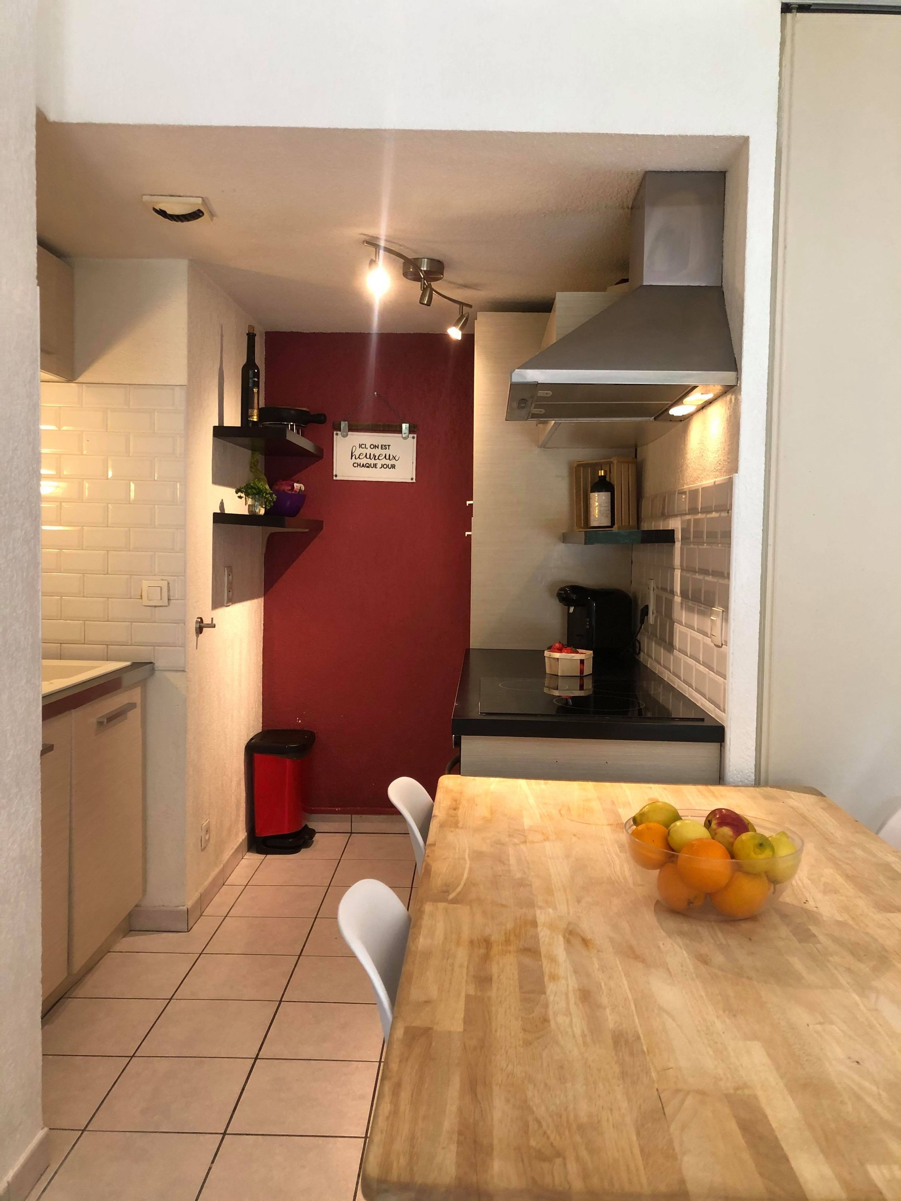 A compact kitchen with a wooden table, a red wall, and a sign.
