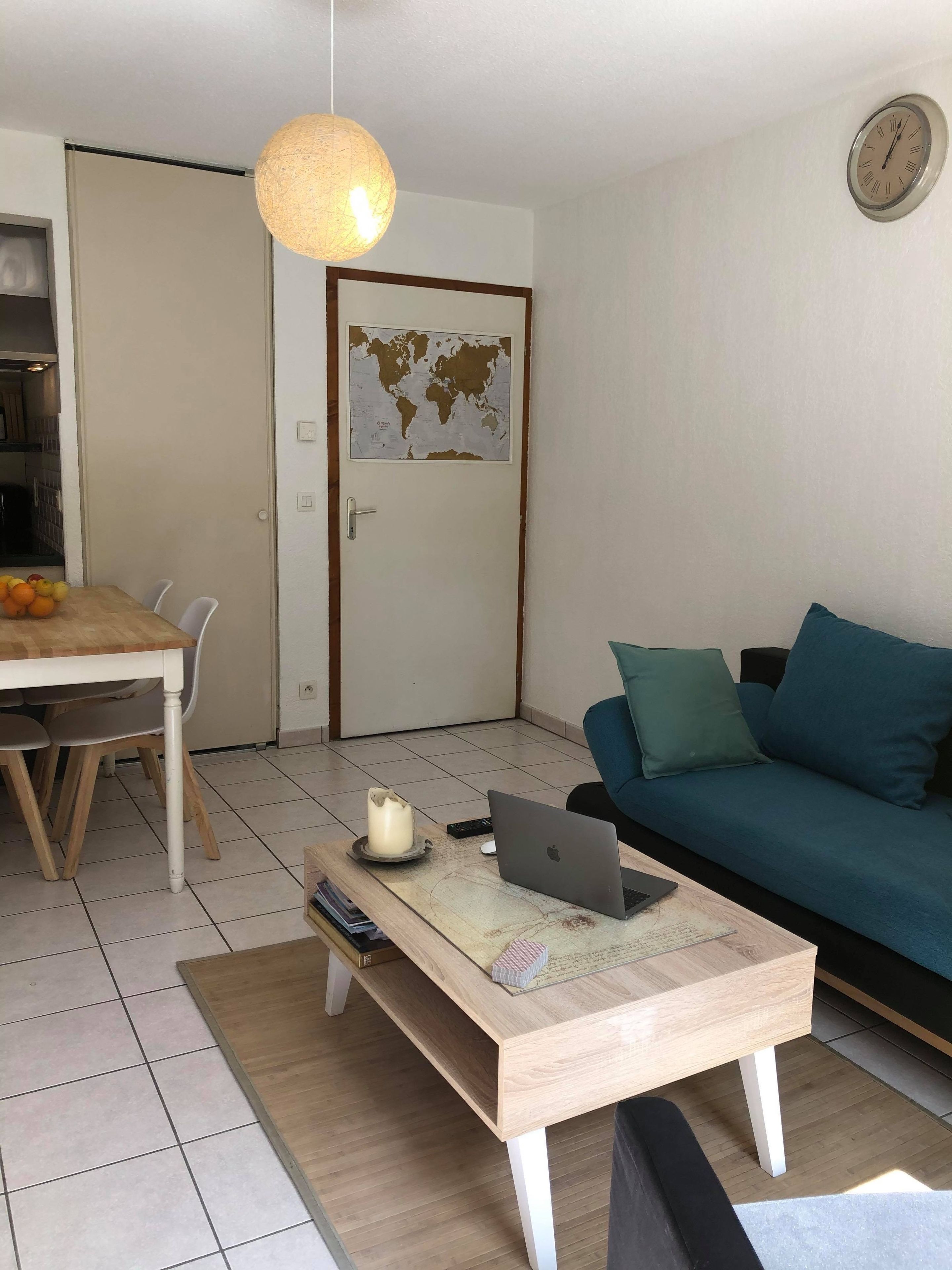 Een woonkamer met een eettafel, een bank, een salontafel met een laptop, een wereldkaart aan de muur en een hanglamp.