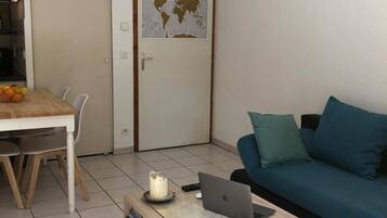 Een woonkamer met een eettafel, een bank, een salontafel met een laptop, een wereldkaart aan de muur en een hanglamp.