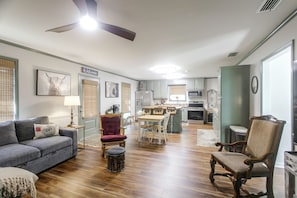 A spacious living area with a sofa, chairs, a dining table, and a kitchen in the background.
