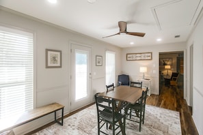 A dining area with a wooden table and chairs, a ceiling fan, and a patterned rug.