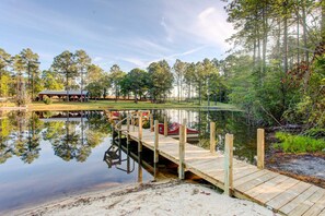 A wooden dock extending into a calm lake, surrounded by trees and a covered area with a boat docked nearby.