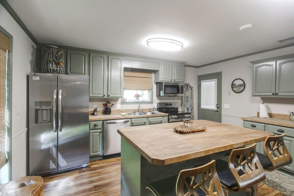 A kitchen with a central island, stainless steel appliances, and wooden chairs.