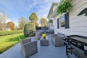 A deck with outdoor furniture and a grill, surrounded by a well-maintained lawn and trees.