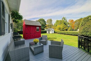 A deck with wicker furniture and a red shed in a garden.