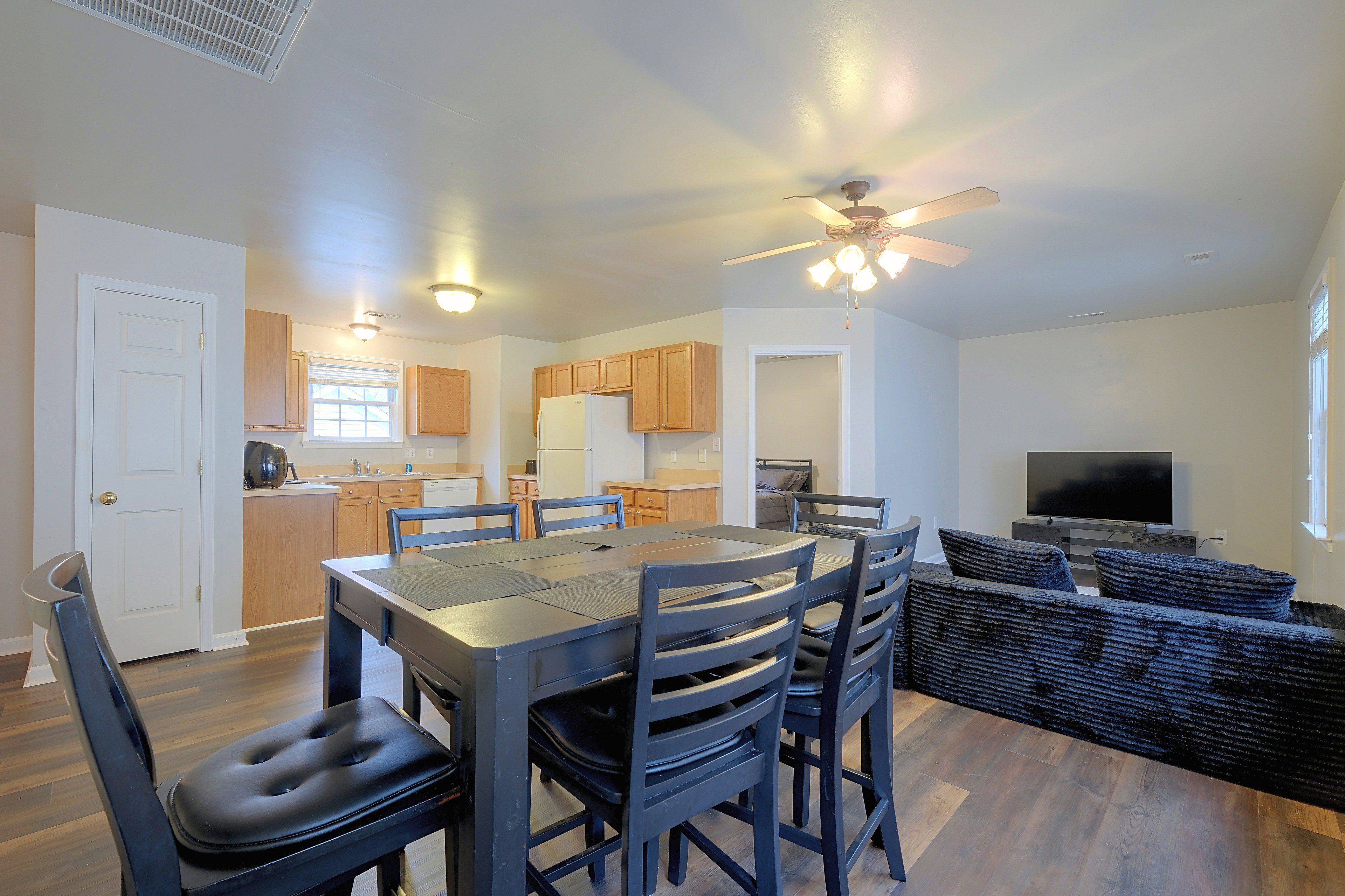 A modern kitchen with wooden cabinets, a dining table with chairs, a ceiling fan, and a television in a living area.