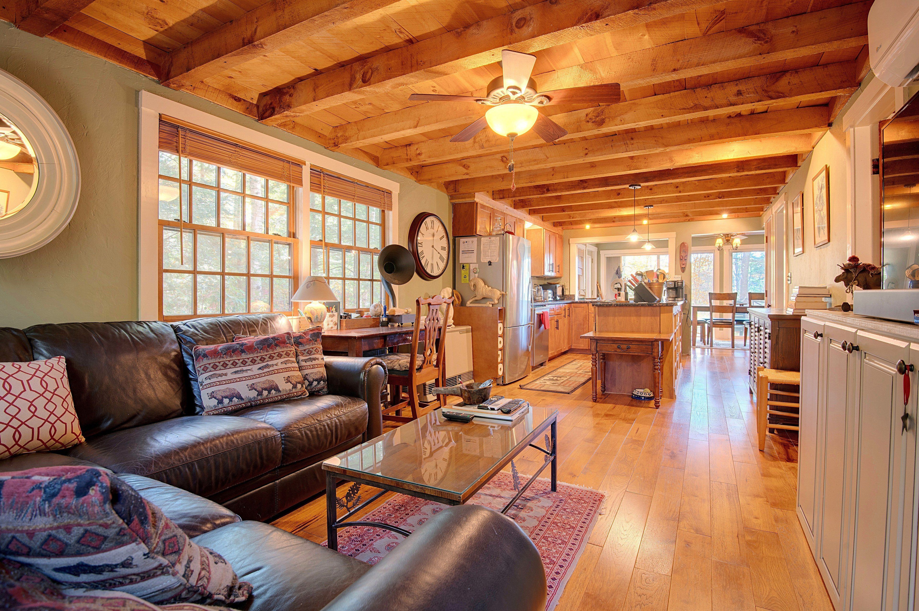 A spacious living room with a leather couch, wooden ceiling beams, and a large window.