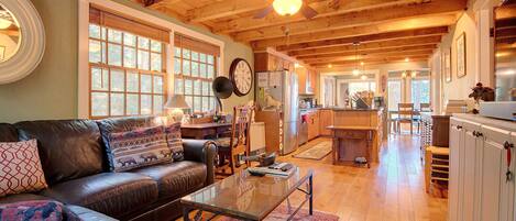 A spacious living room with a leather couch, wooden ceiling beams, and a large window.