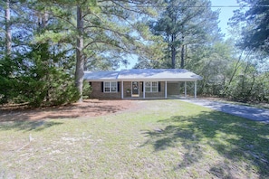 A single-story house with a metal roof, surrounded by trees and a grassy yard.