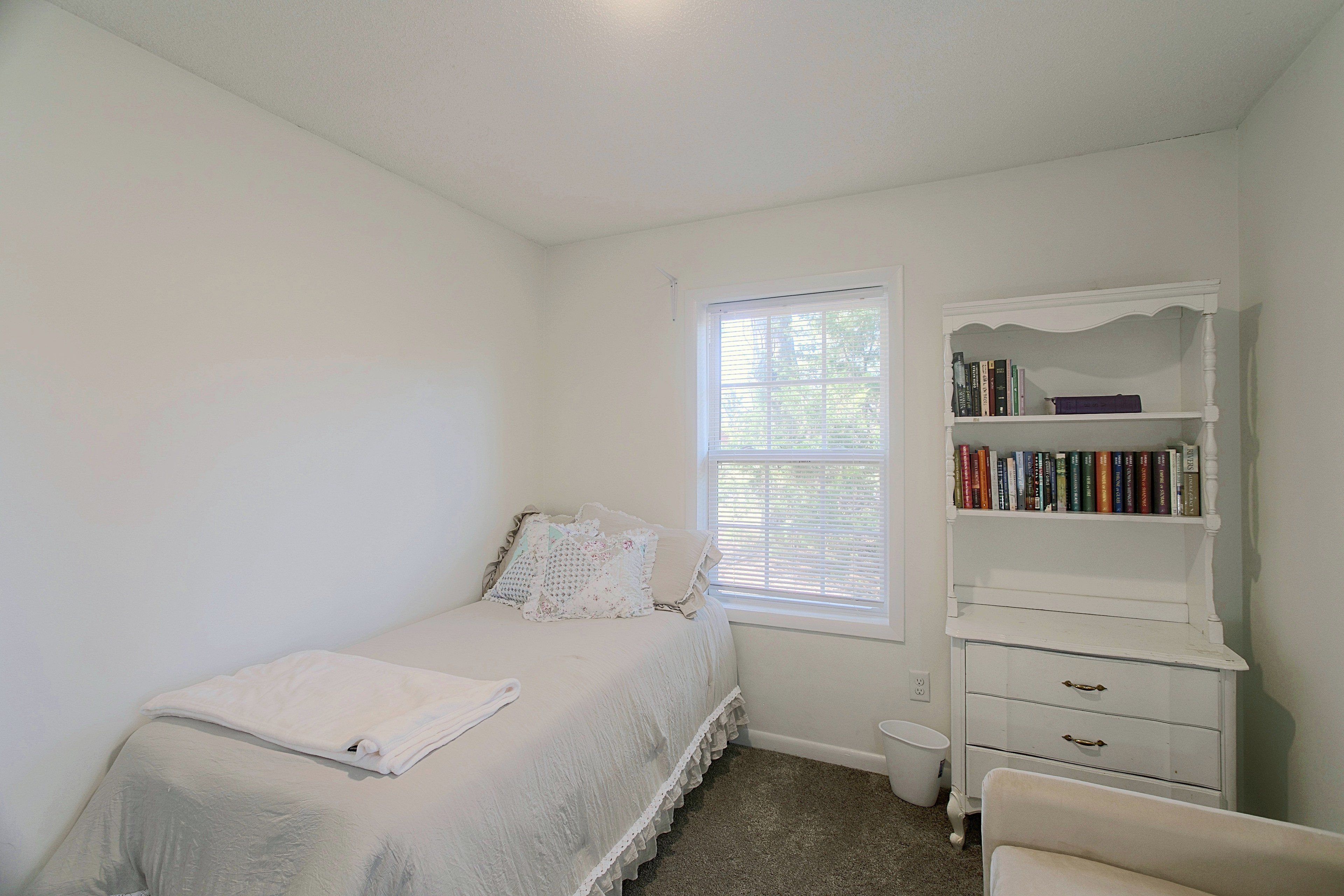 Un dormitorio con una cama individual, un aparador blanco y una ventana con persianas.