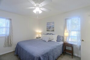 A bedroom with a bed, two bedside tables with lamps, a ceiling fan, and a window with curtains.