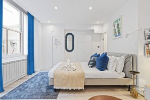 Een moderne slaapkamer met een bed, nachtkastje, lamp, raam met gordijnen en een muur met een lijstwerkfoto.