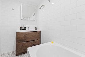 Un baño moderno con azulejos blancos tipo metro, un mueble de tocador de madera, un espejo y una bañera.