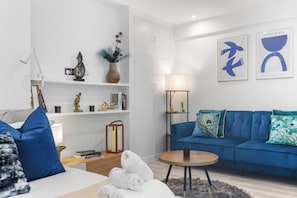 A modern living room with a blue sofa, a round coffee table, and a bookshelf. - Bright & Stylish London Studio | Full Kitchen | Near Hyde Park (London)