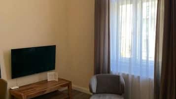 Ein Wohnzimmer mit einem Flachbildfernseher, einem Glastisch, einer Couch und einem großen Fenster mit Vorhängen.
