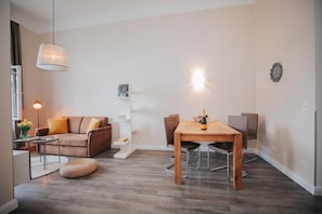 A modern living room with a brown sofa, a wooden dining table, and a pendant light. - Apartments Universitaet by ALPAMI (Wien)