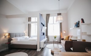 A modern hotel room with a bed, bedside table, lamp, and a seating area with a sofa and a small table. - Apartments Universitaet by ALPAMI (Wien)
