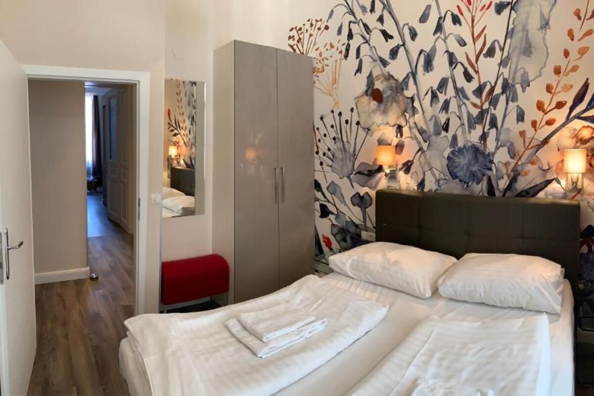 A hotel room with a bed, a wardrobe, a mirror, and a floral wall mural.