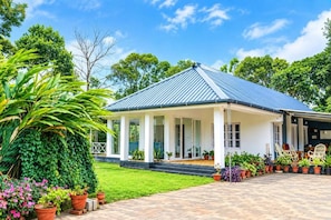 A house with a covered porch, a garden with potted plants, and a clear blue sky. - Thondiyar Estate Bungalow By LexStays (Vandiperiyar)