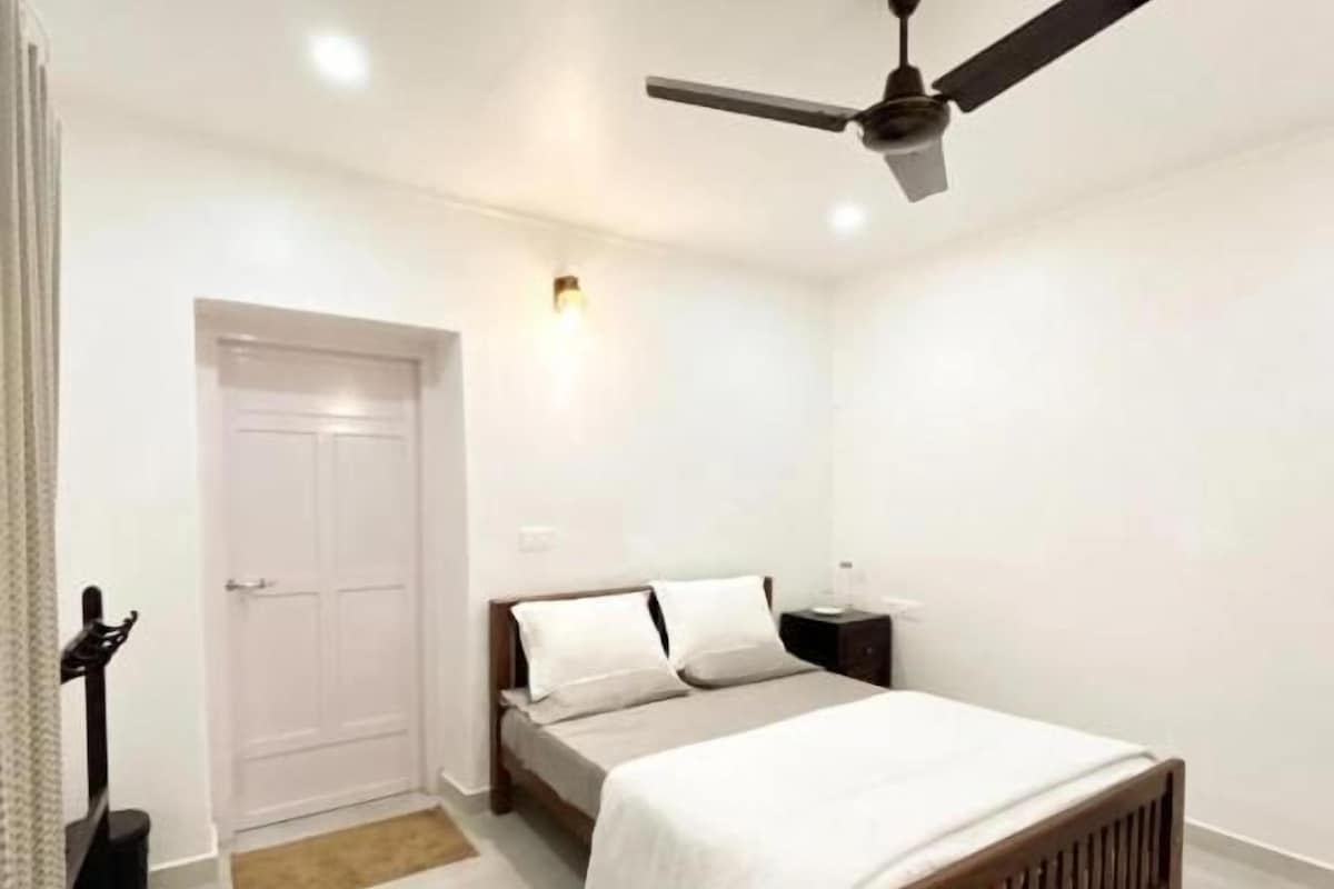 A bedroom with a bed, a ceiling fan, a nightstand, and a door.