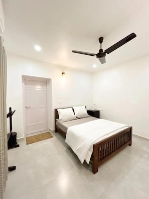 A bedroom with a bed, a ceiling fan, a nightstand, and a door. - Thondiyar Estate Bungalow By LexStays (Vandiperiyar)
