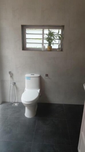 A bathroom with a toilet, a window, and a potted plant. - Thondiyar Estate Bungalow By LexStays (Vandiperiyar)