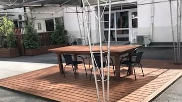 An outdoor patio with a wooden table and chairs, a transparent roof structure, and a white building in the background.