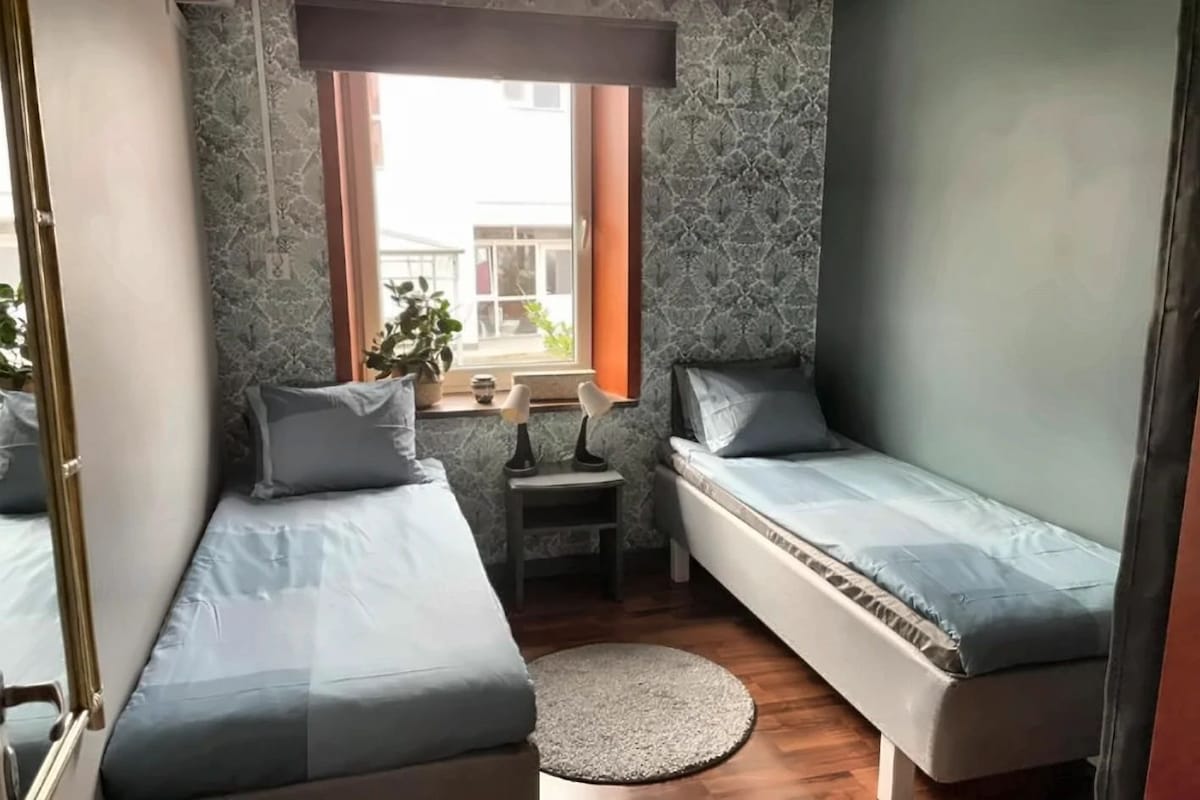 Et lille værelse med to enkeltsenge, et lille bord, et vindue og en plante.
