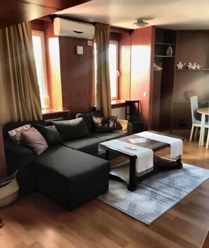 A modern living room with a sectional sofa, a coffee table, and a dining area with a table and chairs. - Astoria Apart Hotel (Skåne län)