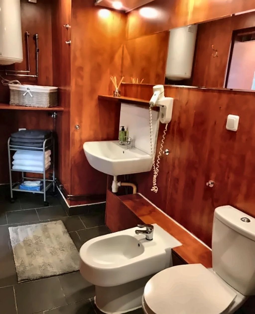 Un baño con pared de madera, un lavamanos blanco, un bidé y un inodoro.