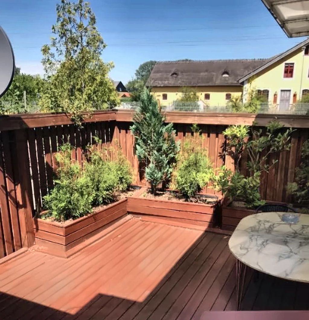 Una terraza de madera con jardineras elevadas, una mesa y vistas a casas al fondo.