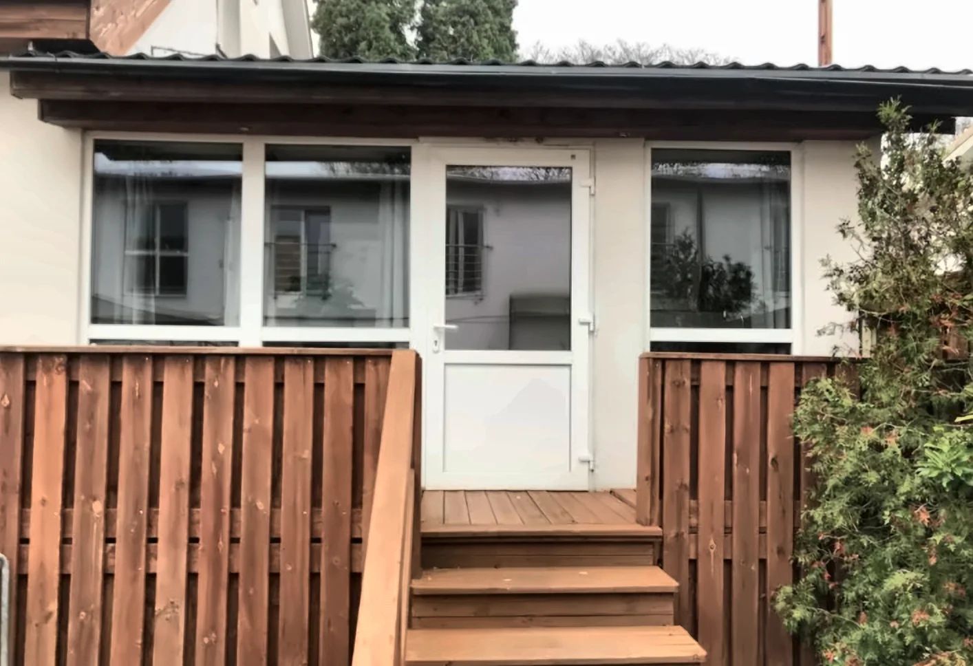 Una terraza de madera que conduce a una puerta blanca con ventanas en la parte superior.