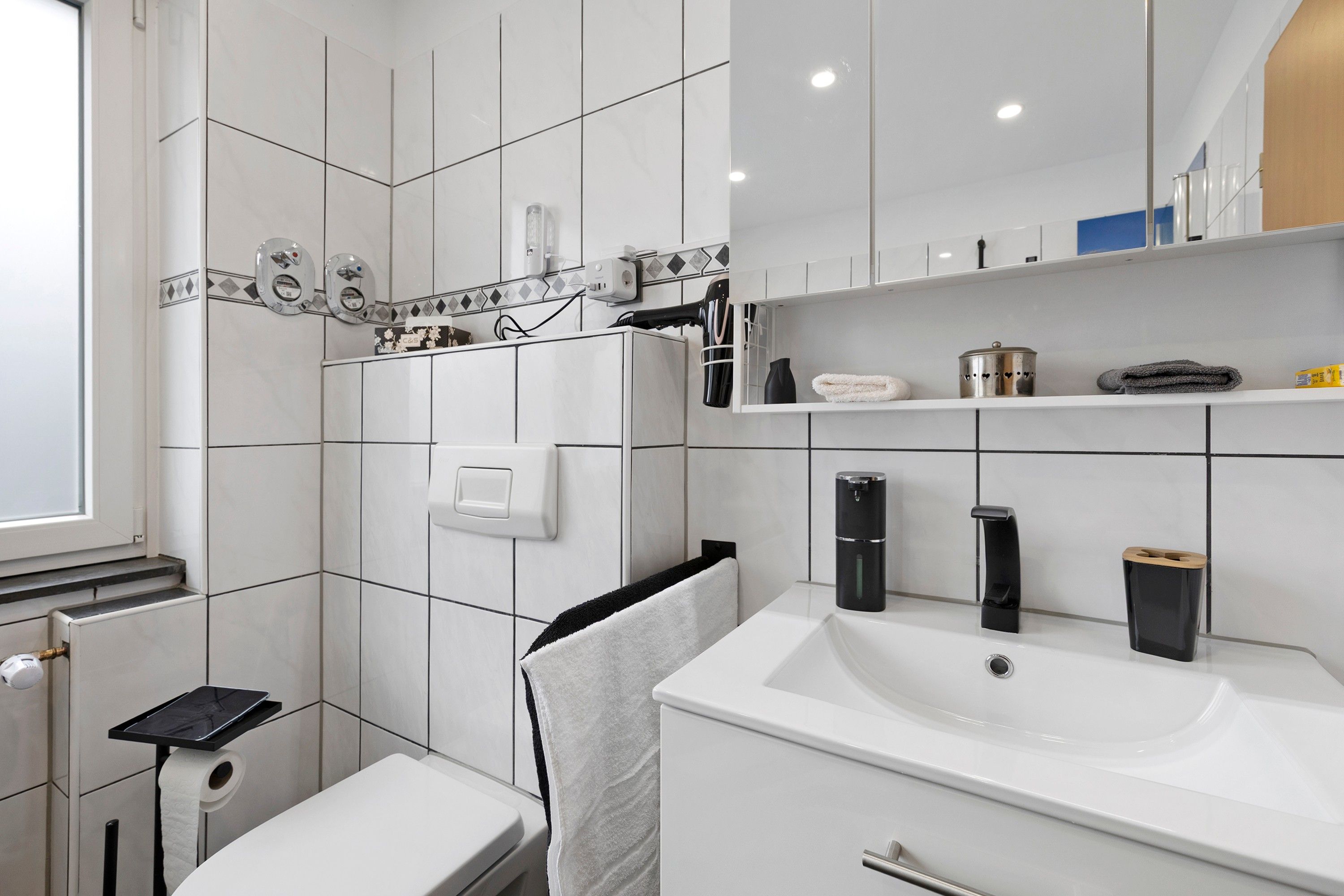 Ein modernes Badezimmer mit einem weißen Waschbecken, einem Handtuchhalter und einer Toilette.