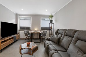 Ein modernes Wohnzimmer mit Flachbildfernseher, einer Couch, einem Couchtisch und einem Essbereich mit Stühlen und Tisch.