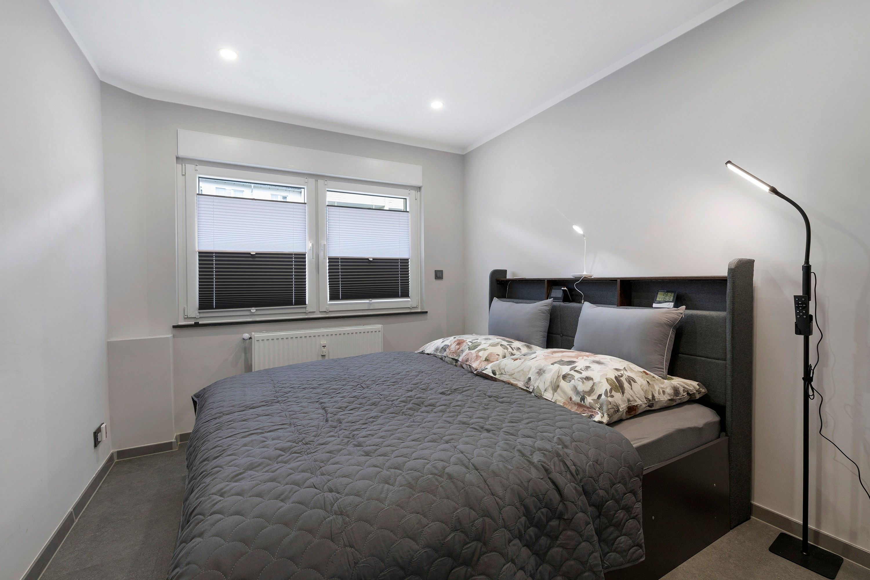 Ein Schlafzimmer mit einem Bett, einem Nachttisch, einer Lampe und einem Fenster mit Jalousien.