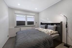 Une chambre à coucher avec un lit, une table de chevet, une lampe et une fenêtre avec des stores.